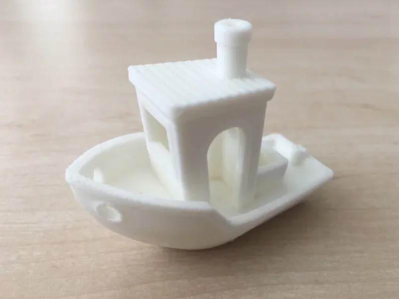 White 3D-printed boat model on wooden surface, created by Raise3D Pro2 Plus printer, showcasing precision in design and build quality.
