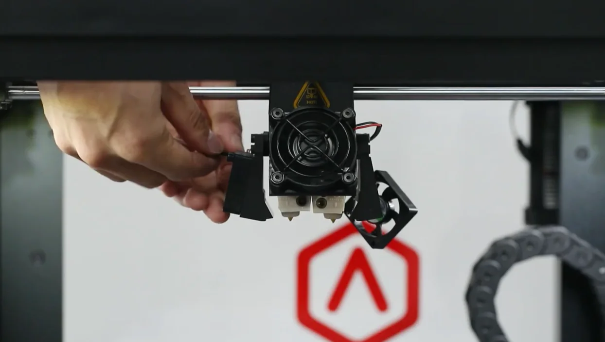 Raise3D Pro2 Plus 3D printer extruder with hand adjusting component, showcasing internal mechanics, branding visible in the background.