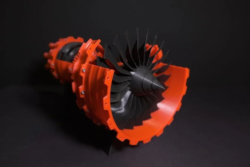 3D printed turbine engine model with black and orange parts created by Raise3D Pro2 Plus, showing intricate fan blades and cylindrical design.