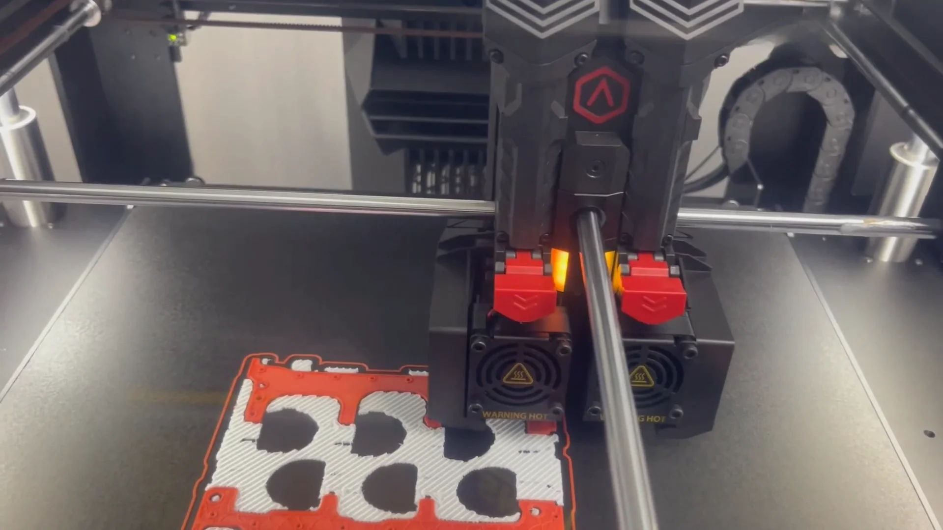 Raise3D Pro3 3D printer operating, creating a red and white component; shows printer nozzle and branding with focus on intricate part details.