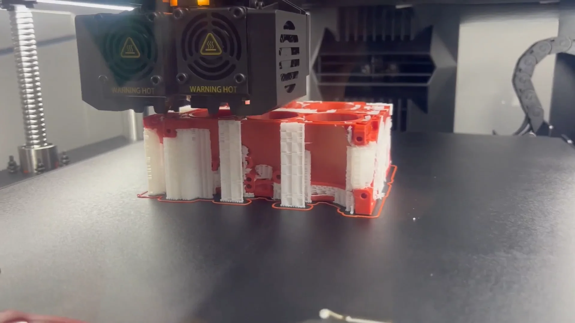 Raise3D Pro3 printing red and white 3D part, showcasing dual extruders and precision engineering.