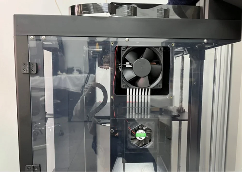 Raise3D Pro3 3D printer internal view, showing cooling fans, wiring, and transparent enclosure; includes printed samples created by the printer.