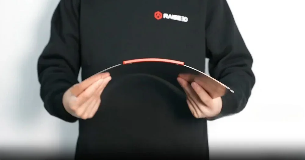 Person holds flexible part created by Raise3D Pro3, showcasing bendability, wearing branded Raise3D black sweatshirt.