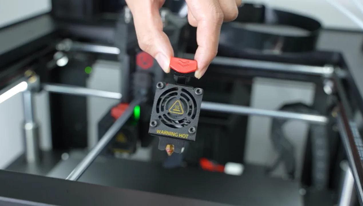 Hand holding a 3D printer extruder nozzle with a red tab labeled "WARNING HOT" in a Raise3D Pro3 printer, emphasizing safety features.