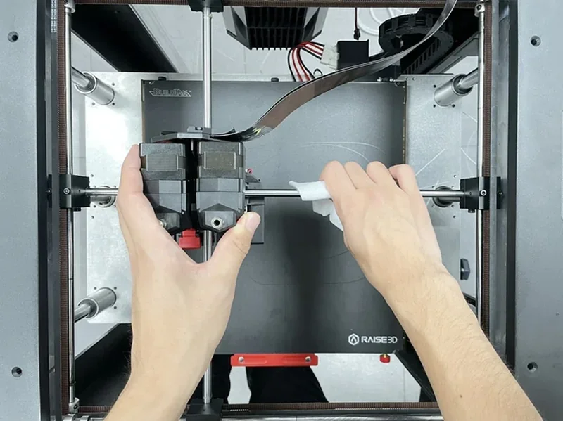 Hands adjusting a Raise3D Pro3 3D printer's components, showcasing its open frame and mechanical parts, with visible branding and internal setup.