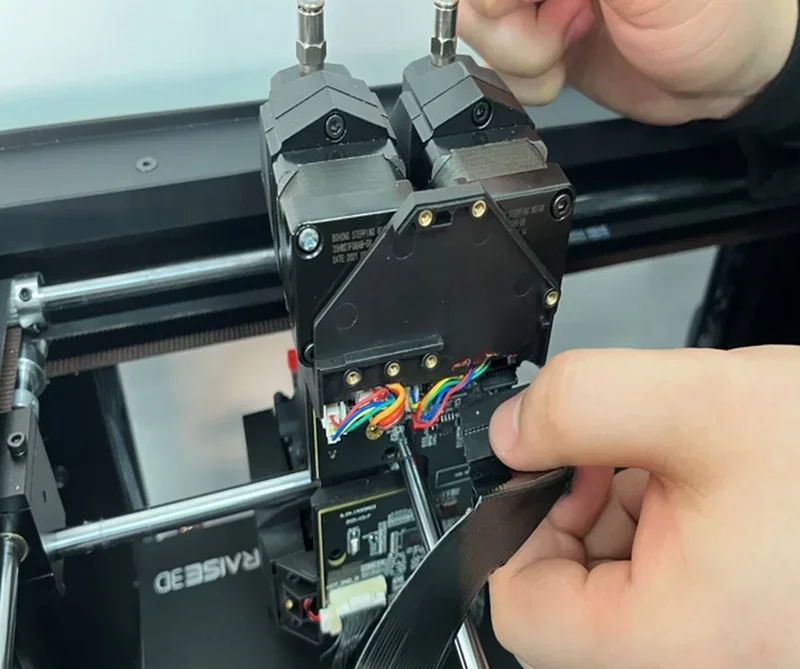 Raise3D Pro3 3D printer detail with wiring adjustments and extruder mechanisms being handled, showcasing its technical components and build quality.