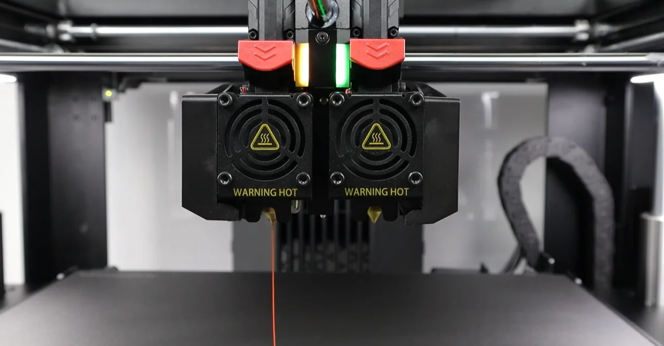 Raise3D Pro3 dual extruders with nozzles, filament, and "Warning Hot" labels, inside a 3D printer, producing sample parts.