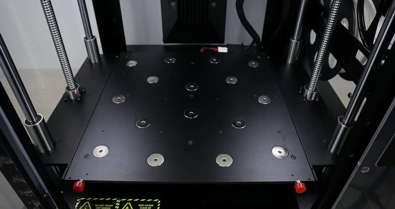 Raise3D Pro3 Plus build platform with metal coil rods and safety warnings, designed for creating precision 3D printed parts.