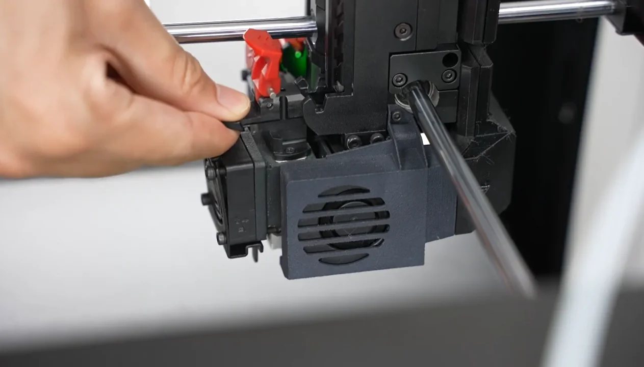 Hand adjusting Raise3D Pro3 Plus 3D printer component with black fan cover during setup, showcasing intricate printer mechanics and design.