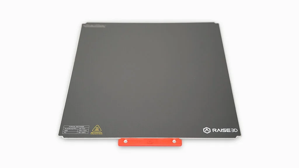 Raise3D Pro3 Plus 3D printer build plate with red clip, logo, and safety markings on a gray surface.