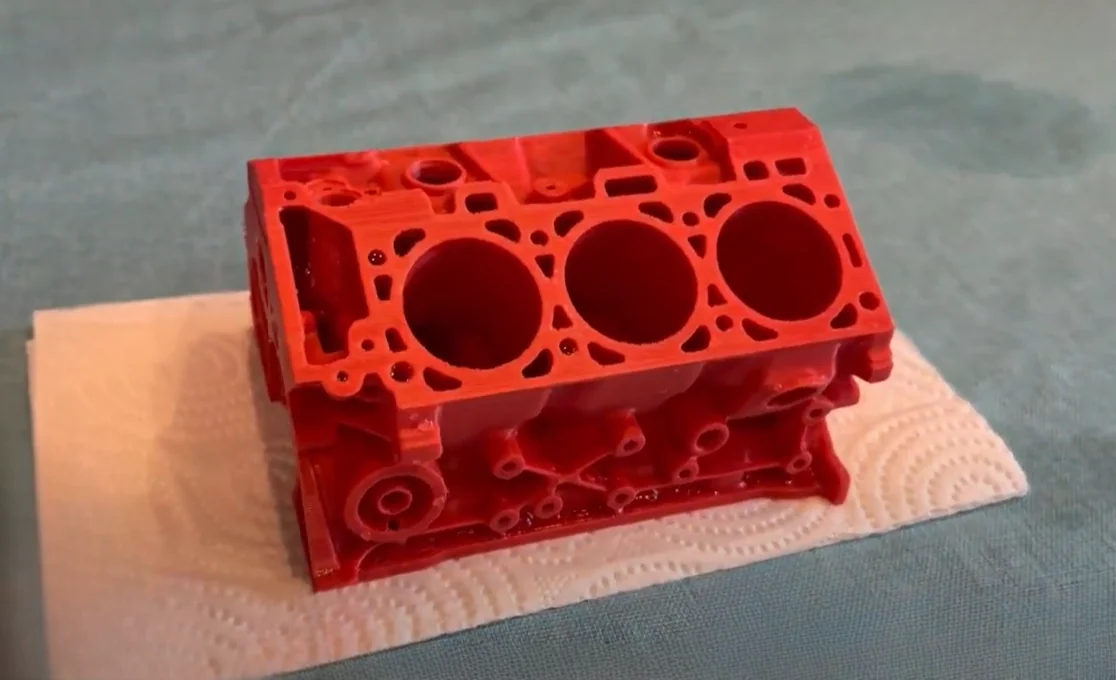 Red 3D-printed engine block on paper towel, created by Raise3D Pro3 Plus, showcasing detailed craftsmanship and design on a blue surface.