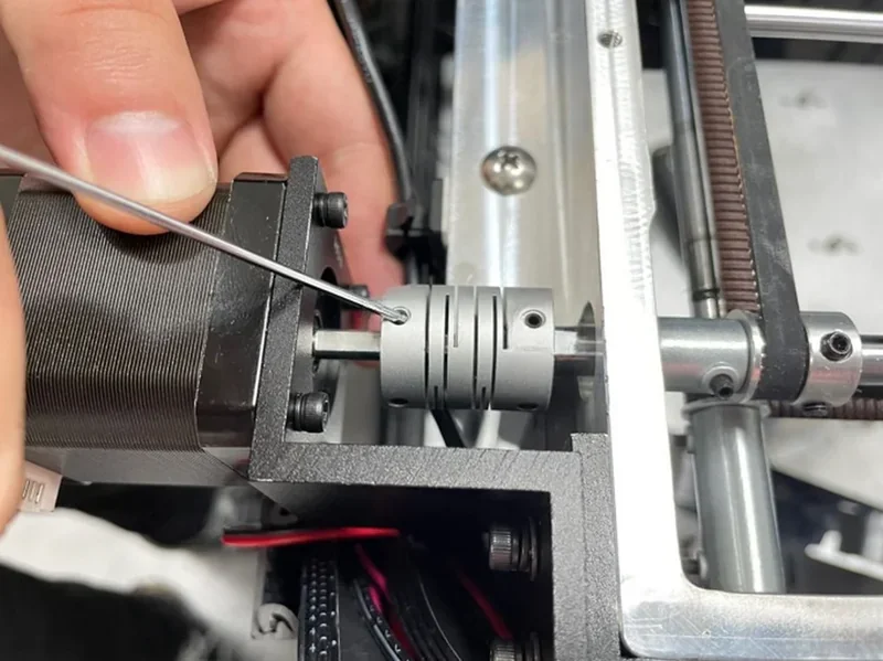 Hand adjusting Raise3D Pro3 Plus 3D printer's motor coupling with wire, showcasing technical maintenance.
