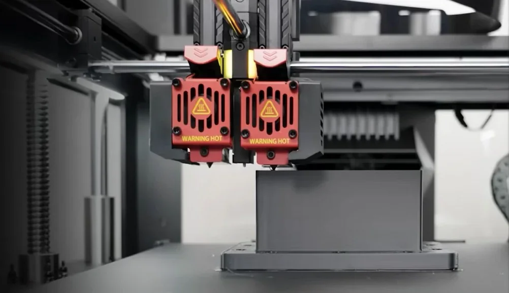 Raise3D Pro3 Plus HS printing with dual extruders on a black object. Branding visible with vented red covers labeled "Warning Hot".