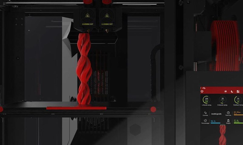 Interior shot of the Raise3D Pro3 Plus HS 3D printer in action, showcasing its printing capabilities. A red, intricately twisted vertical structure is being printed on the build plate, illustrating high-resolution output. The machine’s dual nozzles are visible at the top with 'Warning Hot' labels for safety. The touchscreen interface on the right displays real-time printing information, including temperature settings and progress indicators.