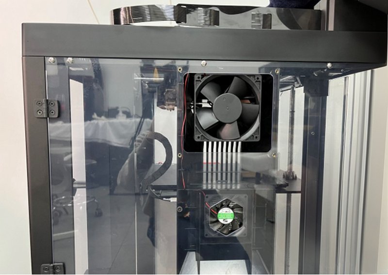 This close-up image details the interior left side of the Raise3D Pro3 Plus HS 3D printer, spotlighting the cooling system. Two fans are prominently mounted on a transparent enclosure, ensuring efficient temperature regulation during printing. The wiring is neatly organized, highlighting the machine’s meticulous internal design. The surrounding glass panels provide a modern, polished look while serving a functional role in maintaining stable environmental conditions.