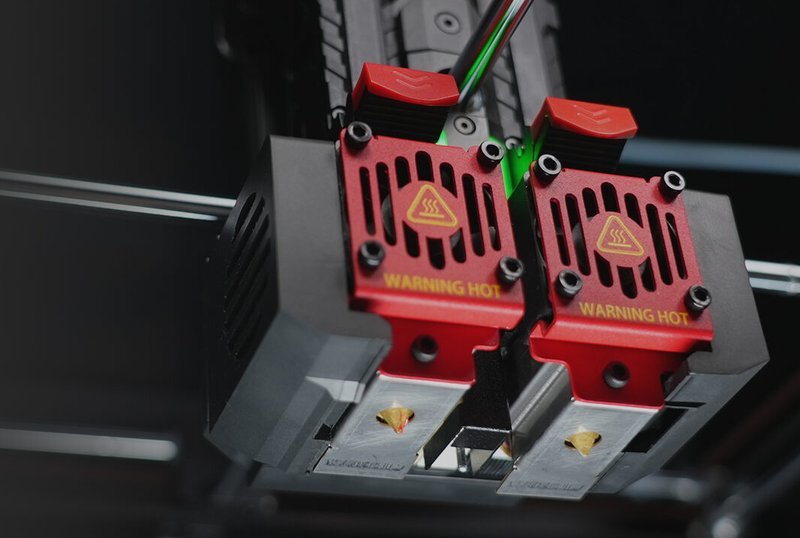 A detailed close-up of the Raise3D Pro3 Plus HS 3D printer's extruder setup. The dual extruders are accented with red components, clearly labeled with 