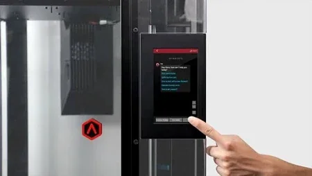 2. Close-up of the Raise3D Pro3 Plus HS dual extruder system in action. The two nozzle heads feature caution symbols and the warning "Warning Hot," mounted on a metal gantry. The extruders are aligned above a red print bed, with a soft-focus background emphasizing the advanced technology of the printer.