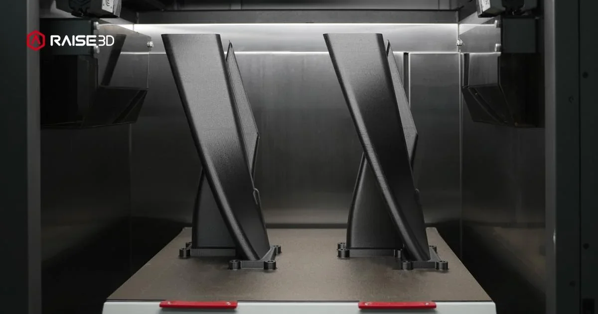 Raise3D RMF500 printing two black parts inside a sleek, illuminated chamber, showcasing precision and advanced 3D printing technology.