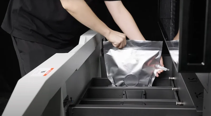 Person handling material inside raise3d rmf500 3D printer, featuring a metallic pouch.