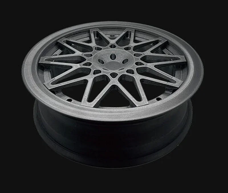 3D-printed intricate black wheel rim, created by Raise3D RMF500 printer, highlighting precise geometric design against a dark background.