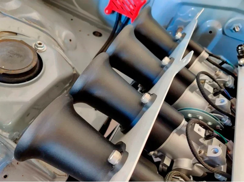 Close-up of engine part components produced by Raise3D RMF500, showcasing precision-crafted black intake manifolds with bolts and wires attached.