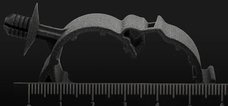 Raise3d RMS220 3D-printed black mechanical part against black background, featuring a scale for size reference.