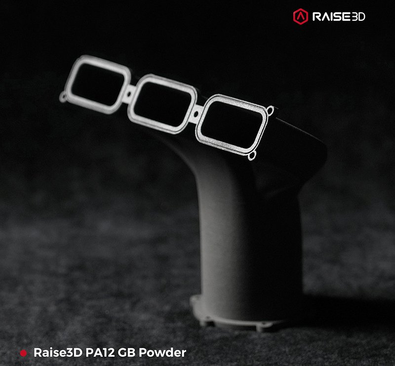 A 3D-printed automotive intake manifold created using Raise3D's PA12 GB Powder, showcasing the intricate design and smooth finish achieved with the Raise3D RMS220 printer. The manifold has a sleek, dark finish and features three rectangular, open-ended ducts, demonstrating the printer's ability to produce precise and complex geometries. The branding 