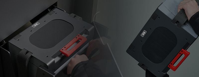 Two views of a component from the raise3d rms220, showing an interchangeable part with a prominent red handle for easy carrying. The matte black surface is accented by the label "SLS" on top, denoting its functionality within the Selective Laser Sintering (SLS) system. The design is practical, with smooth edges and sturdy construction, suitable for frequent handling and replacement.