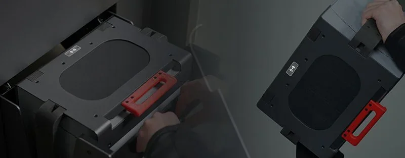 Raise3D RMS220 3D printer tray with red handle, removed by hand, highlighting parts likely created by the printer in a dark, industrial setting.