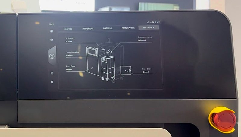 Close-up view of the Raise3D RMS220 3D printer's control panel, highlighting its interface. The touchscreen displays detailed system status, including sections like heaters, movement, material, atmosphere, and interlock. A technical diagram of the machine is shown, displaying the layout and status of sensors and doors, marked as 