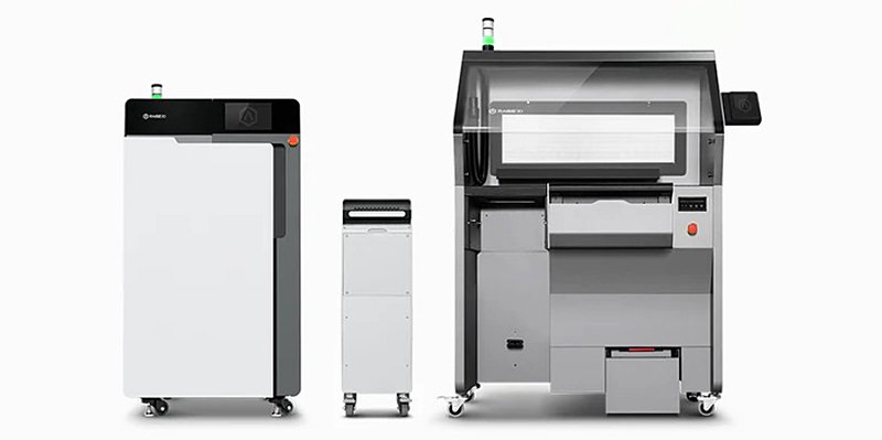 A side-by-side view of the Raise3D RMS220 3D printer and its accompanying components. The printer features a sleek, modern design with a large transparent chamber for printing, adjustable digital controls, and a prominent control button. To its left is a processing unit with a similar aesthetic, including a black top and a white body, designed with mobility features such as caster wheels. Branding is visible, showcasing an industrial-grade setup suitable for advanced manufacturing environments.