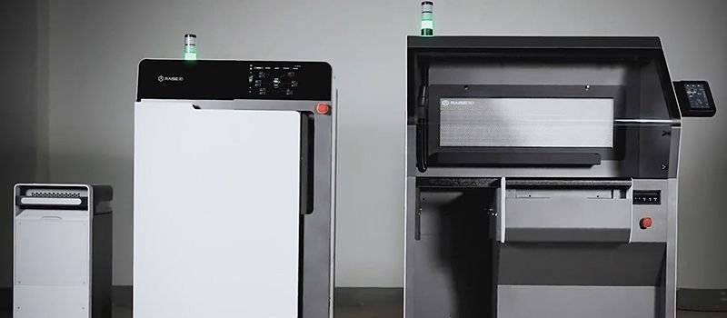 A comparison image featuring three Raise3D devices, including the Raise3D RMS220. The devices are positioned in a well-lit, minimalistic studio setting. The RMS220 is identifiable by its distinct control panel and display screen, with a sleek, modern design that emphasizes industrial use. Visible branding and LED indicator lights on top of each unit suggest operation status, enhancing the professional appearance of the lineup.