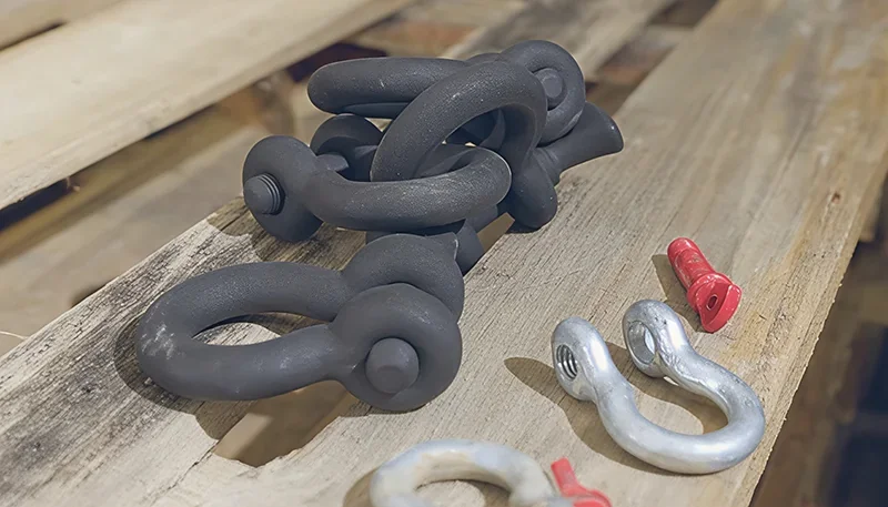 Sinterit Lisa X 3D-printed black shackles on a wooden surface alongside metal shackles and red pins, highlighting precision and detail.