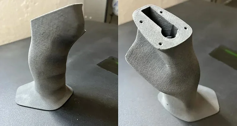 3D-printed part created by Sinterit Lisa X, showcasing a smooth, contoured structure on a dark surface, highlighting precision and detail.