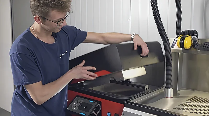 Sinterit Lisa X 3D printer being operated by a person, showcasing a sleek design with control panel; parts created by the printer are included.