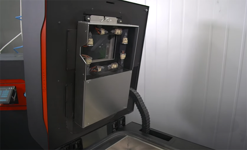 Sinterit Lisa X 3D printer with open door showing internal mechanism and control panel, set in a modern industrial environment.