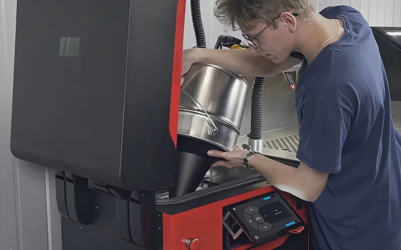 Sinterit Lisa X in use; person loads powder into a sleek 3D printer. Product design and operating interface visible, showcasing additive manufacturing.