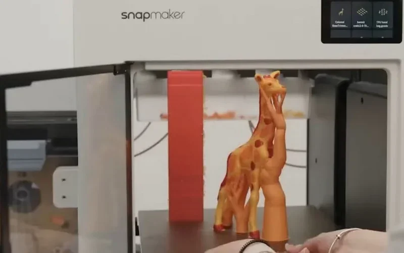 Snapmaker u1 3D printer open with a detailed giraffe figure inside, hand adjusting; giraffe model created by the printer, visible screen interface.