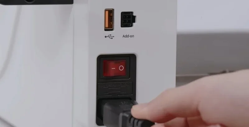 Snapmaker U1 power switch and ports with hand plugging in cable; features USB and add-on connections on a white panel.