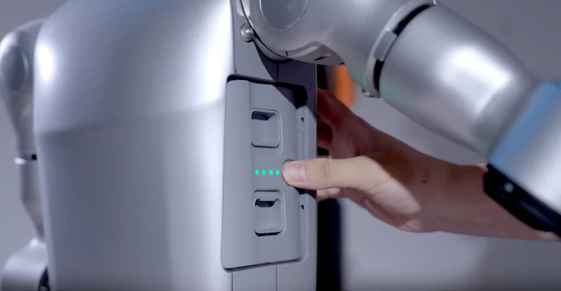 Unitree G1 robot's arm interacts with a grayscale device, featuring illuminated indicator lights, in a tech setting.