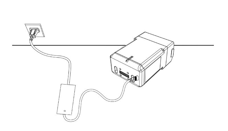 A technical line drawing depicting the setup of an electronic device connected to a power source. The device is connected with an integrated cable leading to an outlet on the left. The configuration includes a small intermediate box, presumably a transformer or power adapter, displaying a streamlined, functional design. The context suggests a component or part associated with a larger robotic system, focusing on power management.