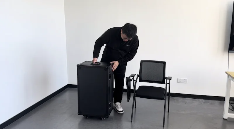 A person adjusts a black case, likely housing the Unitree G1, beside a chair in a minimalist room.