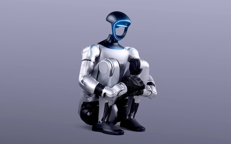 The Unitree G1 humanoid robot is shown in a squatting position against a neutral gray background. It features a sleek, futuristic design with a metallic silver body and black accents. The robot's head is smooth and helmet-like, with a glowing blue line where the face would be, adding to its advanced appearance. The articulation of its joints, visible in the knees and elbows, suggests a high level of mobility, emphasizing its humanoid characteristics.