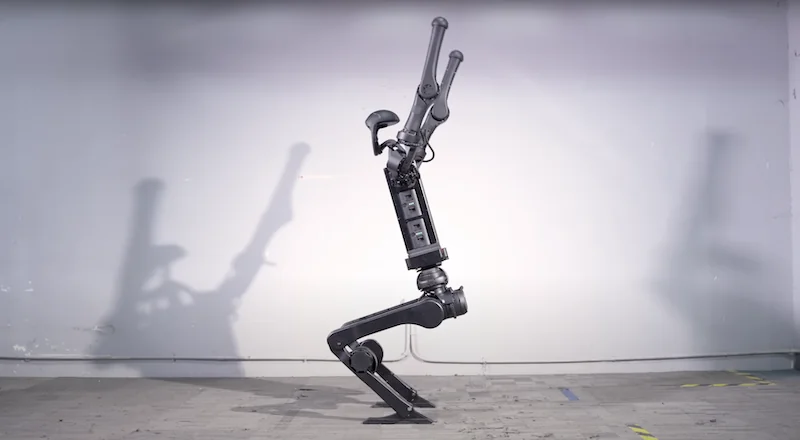 Unitree H1 robot in an indoor setting, depicted in profile with articulated limbs and sleek design, casting shadows on the floor and wall.